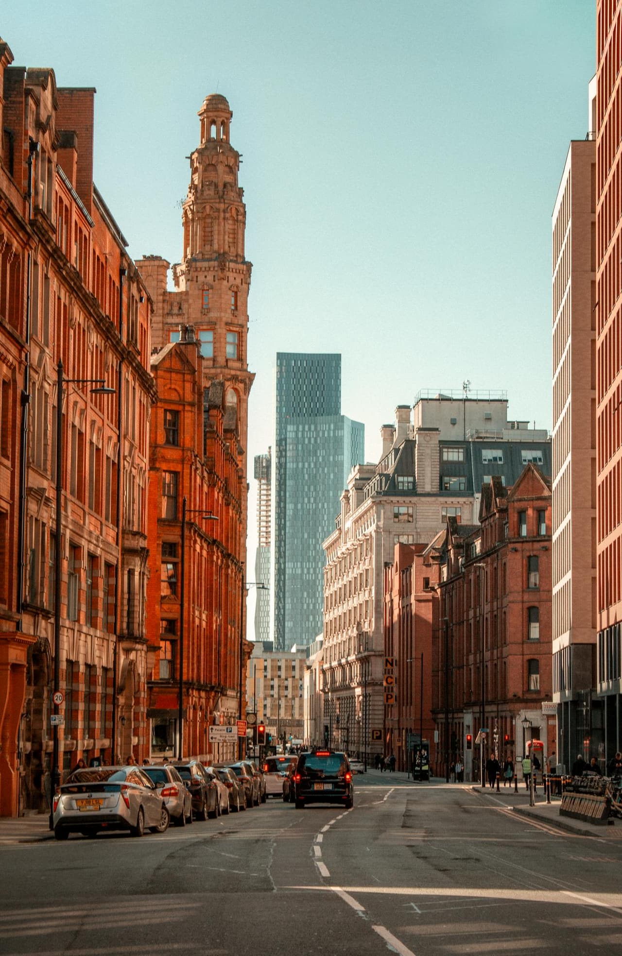 A sunny Manchester street with historic and modern architecture in contrast.