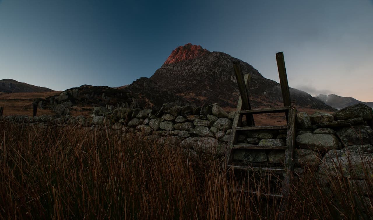 Beautiful twilight view of Tryfan mountain with stone wall and ladder in a rural setting.